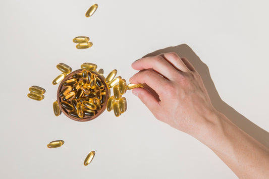Hand holding omega-3 fish oil capsules in wooden bowl for heart and brain health